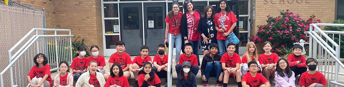Fourth grade students in red shirts with principal and teachers on front steps