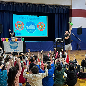 Students and adults in gym with their hands up