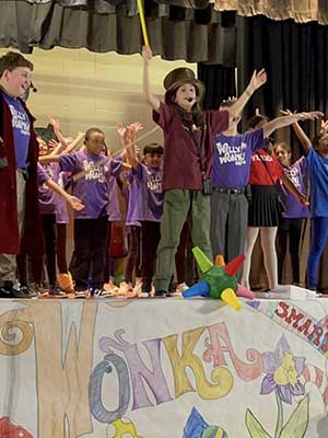 Students with hands in the air on a stage with the word Wonka on it