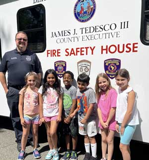 Students and officer standing in front of a Fire Safety House