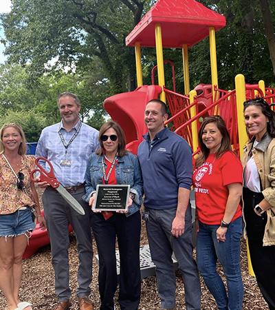 Adults on the playground holding a plaque and large scissors