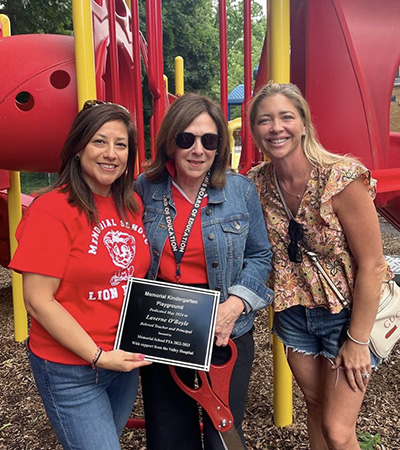 Three adults on the playground holding large scissors and a dedication plaque